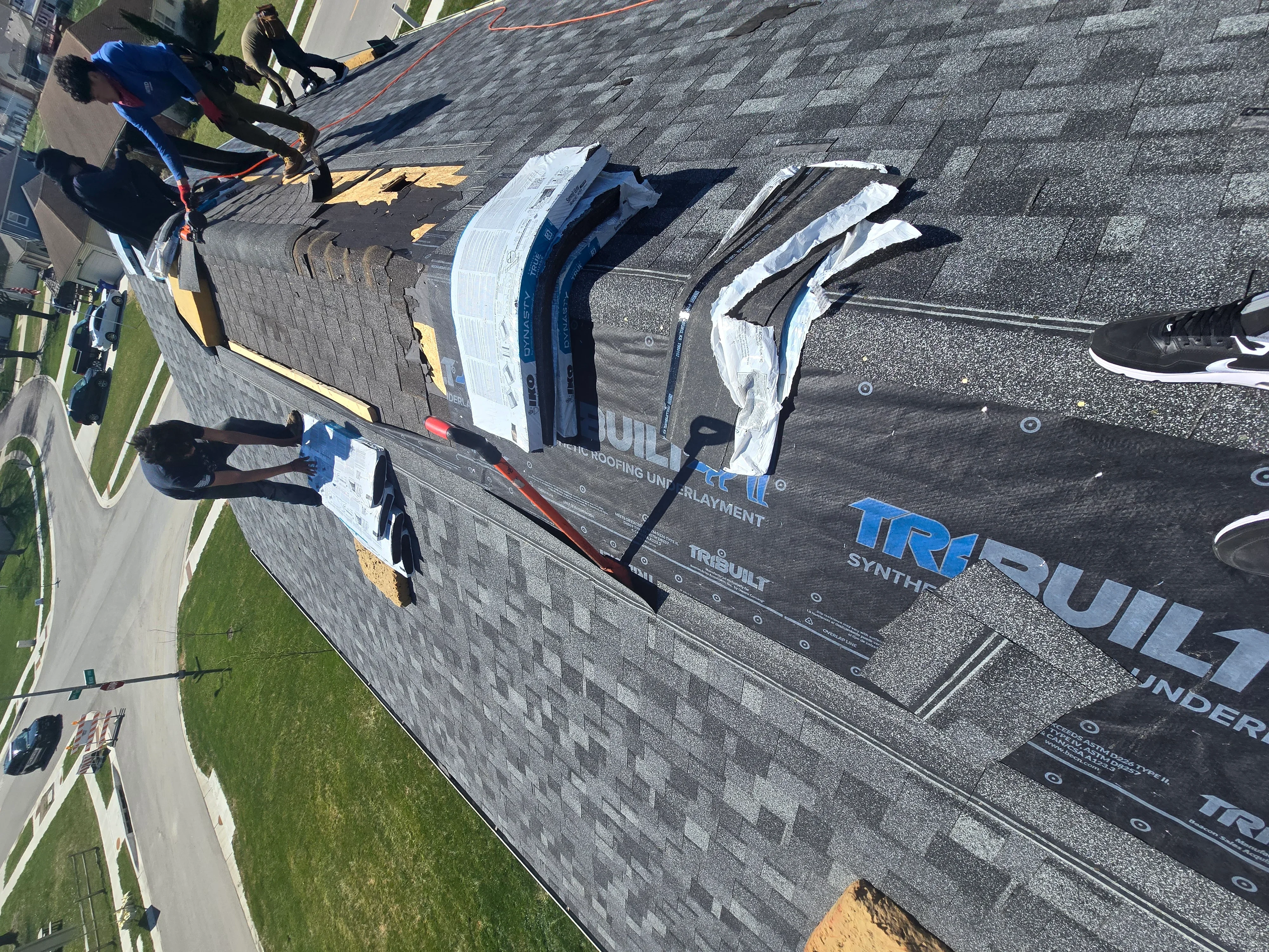 Roofers installing gray architectural shingles with white underlayment and ice shield on pitched roof