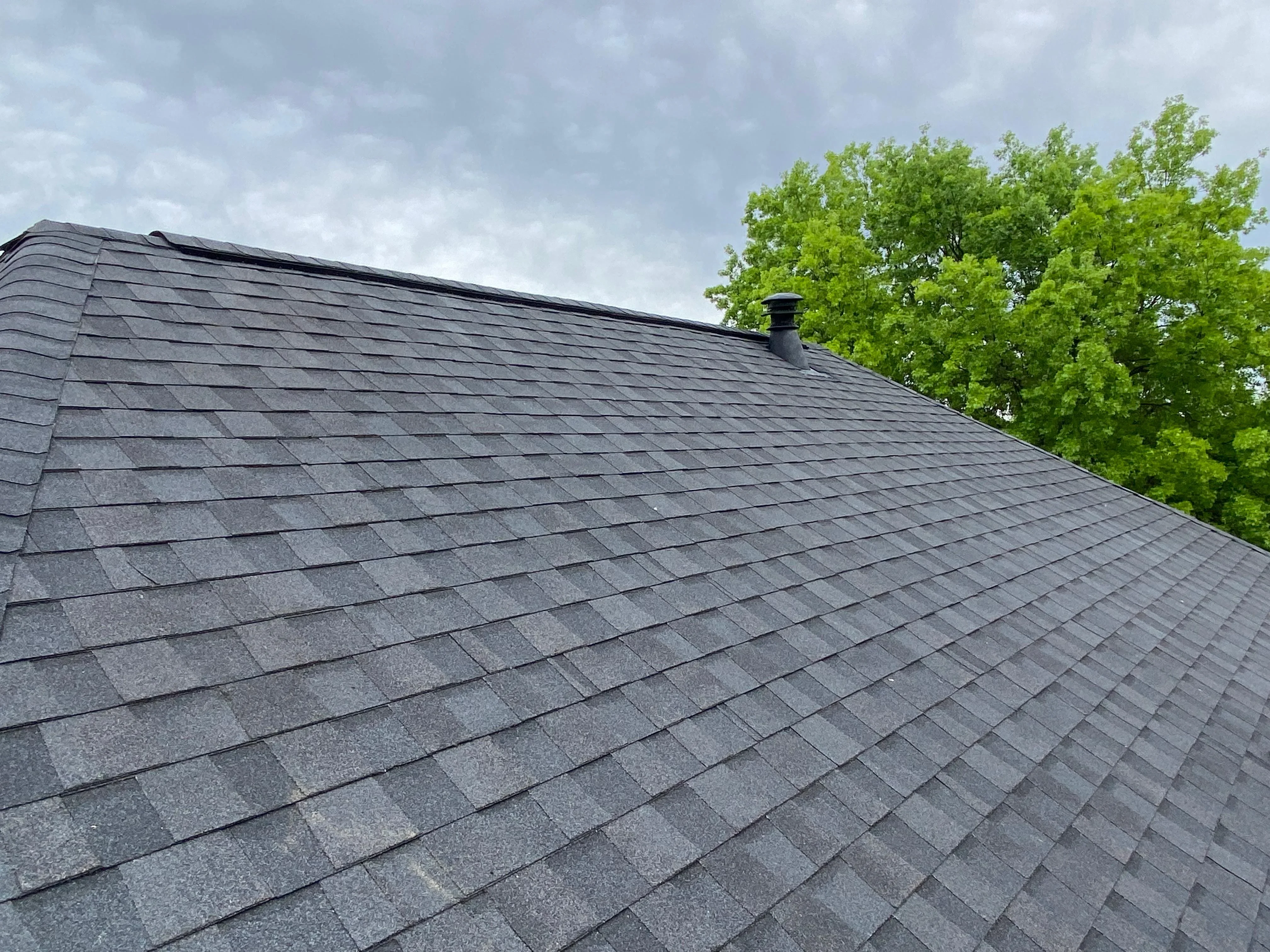 Charcoal gray architectural shingles installed on pitched roof with chimney flashing