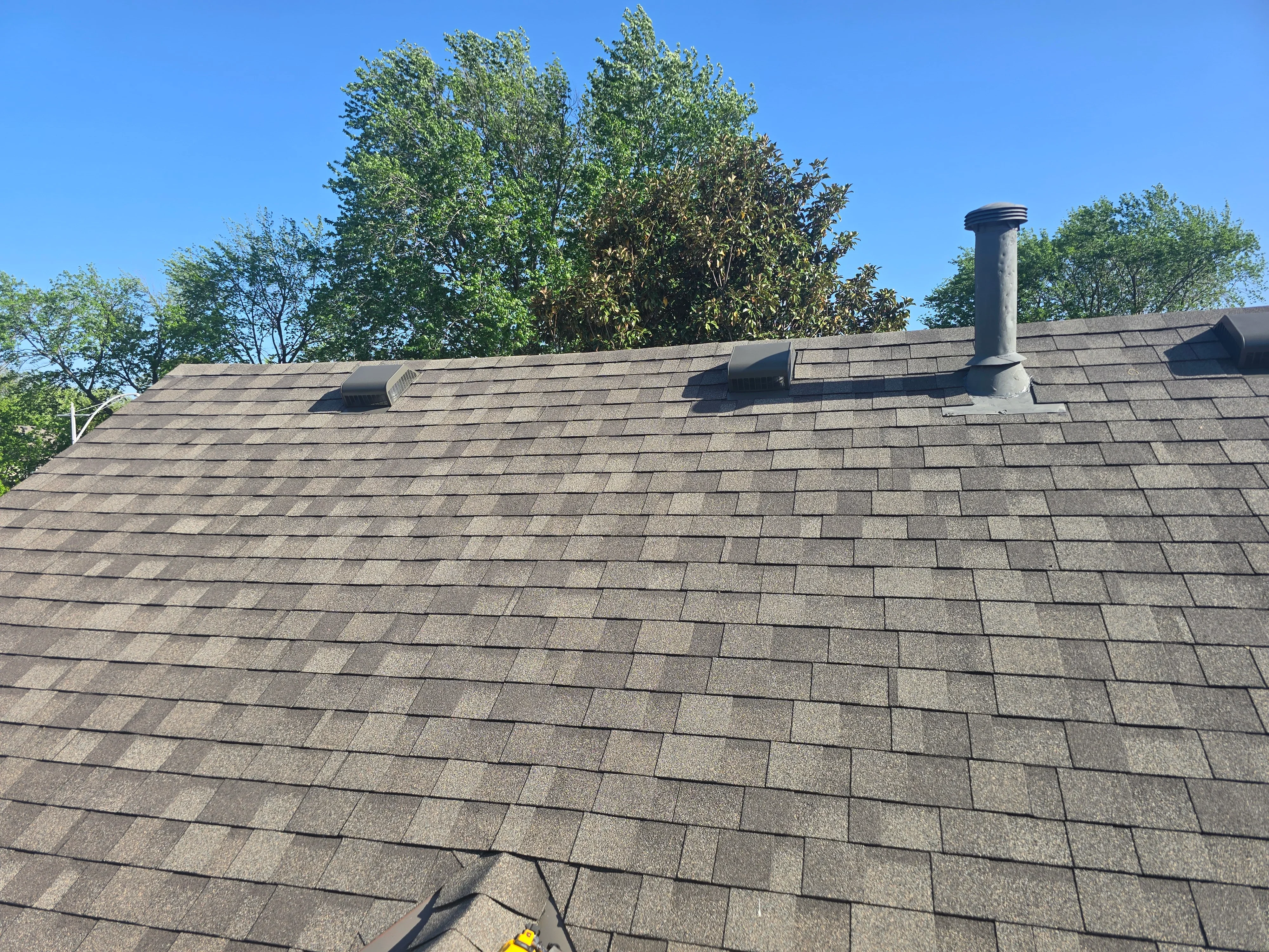 Charcoal gray architectural shingles with ridge vents and chimney chase on completed roof installation