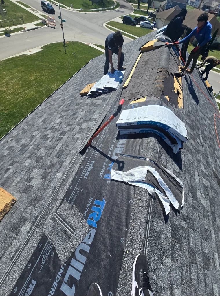 Crew installing gray asphalt shingles on residential pitched roof with safety equipment