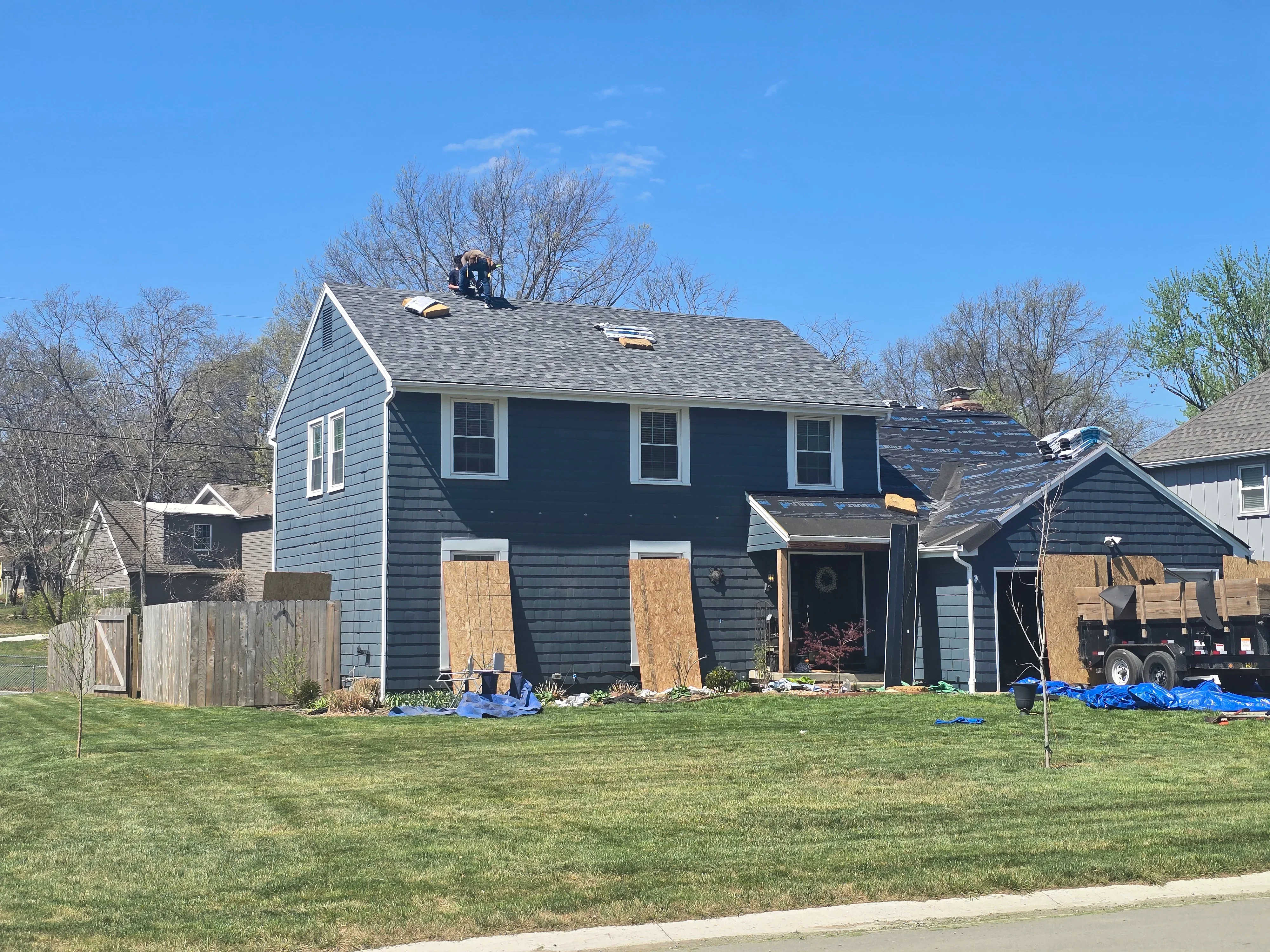 Two-story home with new gray asphalt shingle roof installation and boarded windows during construction